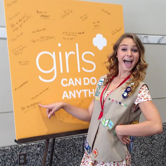 Girl Scout posing with "Girls Can Do Anything" sign.