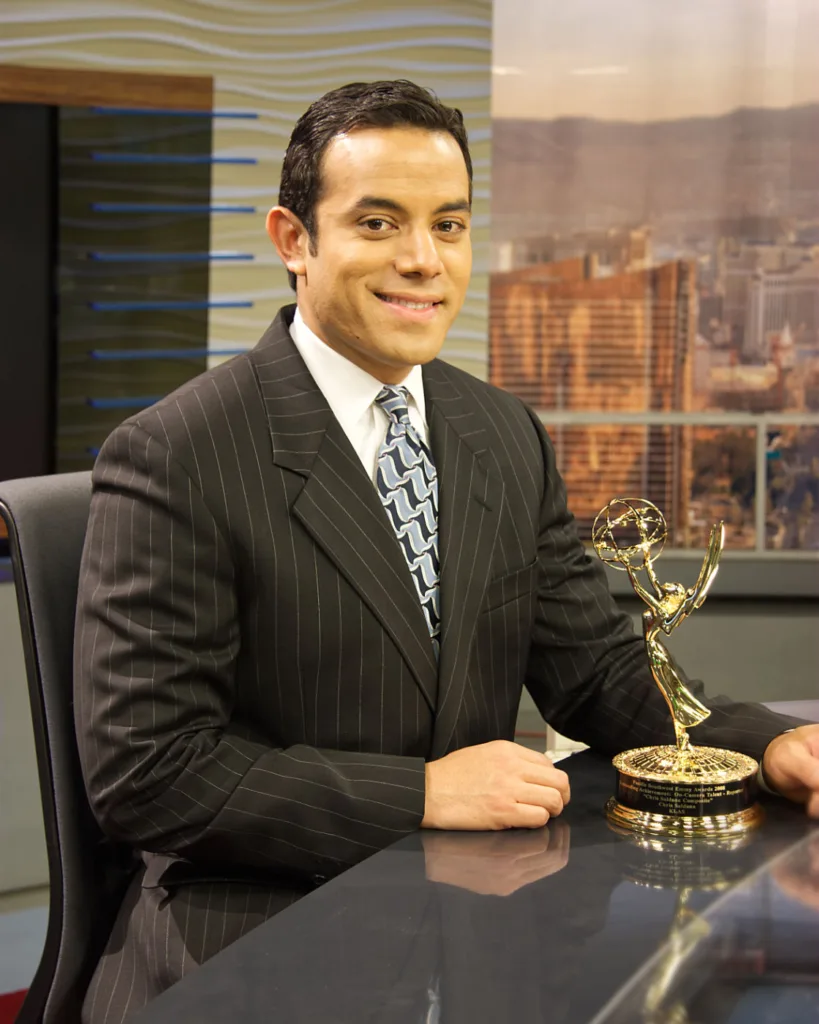 Broadcaster smiling with Emmy Award in studio.