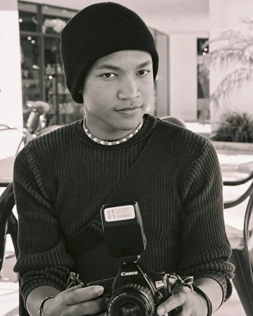 Young photographer holding camera, wearing beanie, black and white photo.